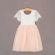 White lace top and pink tulle skirt dress on a hanger against a gray background