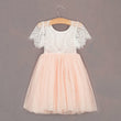 White lace top and pink tulle skirt dress on a hanger against a gray background