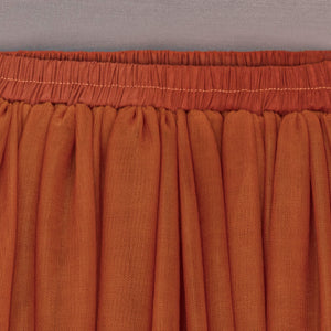 Close-up of a rust-colored fabric skirt with an elastic waistband.
