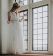 girl in a white dress standing by a large window