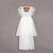 White dress with ruffled straps on a wooden hanger against a gray background