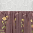 Embroidered floral pattern on a brown fabric against a textured white background