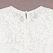 Close-up of a white lace garment with pearl buttons on a beige background