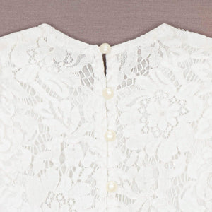 Close-up of a white lace garment with pearl buttons on a beige background