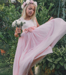 Young girl in a pink dress with floral headband and bouquet, standing in a garden.