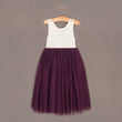 White lace top and purple tulle skirt dress on a hanger against a brown background