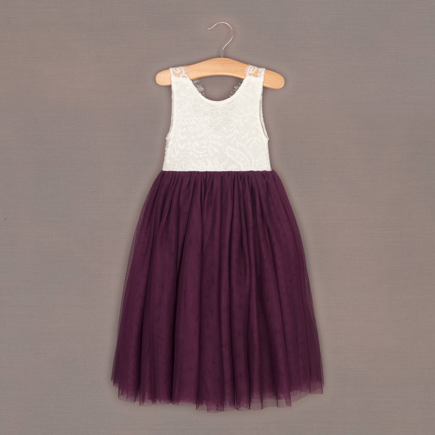 White lace top and purple tulle skirt dress on a hanger against a brown background