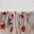 Close-up of a sheer white tulle skirt with embroidered orange and red flowers and green stems, layered over a white lace fabric.
