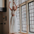 Girl in a white lace outfit standing in a room with large windows.