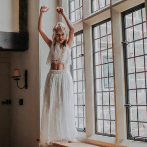 Girl in a white lace outfit standing in a room with large windows.