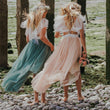 Two girls in flowing dresses walking on a rocky path on the beach