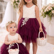 Two young girls in matching dresses with burgundy skirts and white tops, holding baskets.
