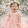 Young baby girl in a pink dress with a floral headband standing in front of a floral arch.