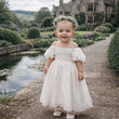Baby girl wearing her Raye dress in pretty stately grounds
