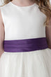 Close up of Ivory dress with a purple belt worn by a child