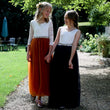 Two girls in formal dresses standing on a gravel path with greenery in the background