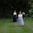Two young girls in formal dresses standing on a grassy area with trees in the background.