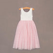 Pink dress with white lace top on a wooden hanger against a brown background