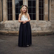 Young girl in a bohemian dress with white top and black skirt standing in front of a stone building.