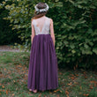 girl wearing a purple dress with a white lace top against a green bush.