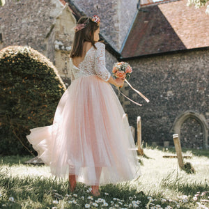 GIRL in a white lace top and blush skirt standing in a garden with a church in the background