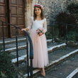 Young girl in a white lace top and BLUSH dress with a flower crown standing on stone steps.