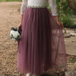 Person wearing a white lace top and purple tulle skirt holding a bouquet outdoors.