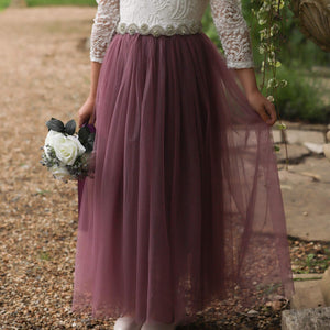 Person wearing a white lace top and purple tulle skirt holding a bouquet outdoors.