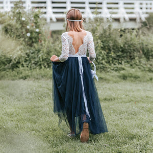 Girl in a lace top and navy blue skirt standing in a grassy field.