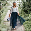 Young girl in a white lace top and blue skirt walking on a path in a garden.