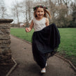Young girl in a white top and black skirt with a flower crown running outdoors.