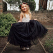 Young girl in a white and black dress with a floral crown outdoors.