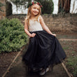 Young girl in a sleeveless dress with lace top and black skirt with a floral headband outdoors.
