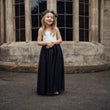 Young girl in a white top and black skirt standing in front of a stone building.