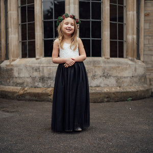 Young girl in a white top and black skirt standing in front of a stone building.