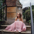 Young girl in a pink dress sitting on steps outdoors with a building in the background