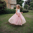 Young girl in a white top and pink dress with a floral headband standing in a garden.