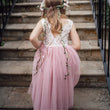 Young girl in a pink dress with floral decorations standing on stone steps.