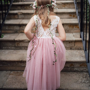 Young girl in a pink dress with floral decorations standing on stone steps.