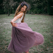Girl in a flowing purple dress with floral headpiece standing in a grassy field.