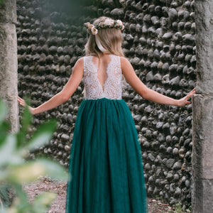 Girl in a green dress with a floral headband standing against a textured stone wall.