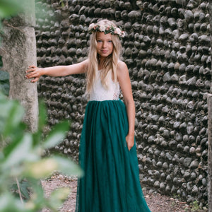 Girl in a white top and green skirt standing against a textured stone wall.