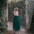 Girl in a white top and teal skirt standing in front of a stone wall.