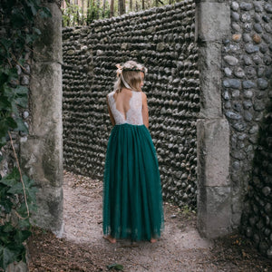 Girl in a white top and teal skirt standing in front of a stone wall.