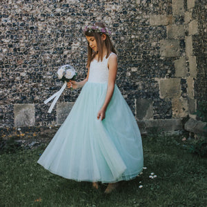 Young girl in a light blue dress standing against a stone wall.