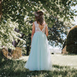 Girl in a light mint blue dress standing in a garden with trees and grass.