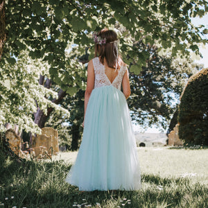 Girl in a light mint blue dress standing in a garden with trees and grass.