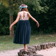Girl in a navy dress with an open back standing on wooden logs in a natural setting