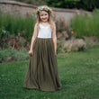 Young girl in a white top and green skirt standing in a garden.