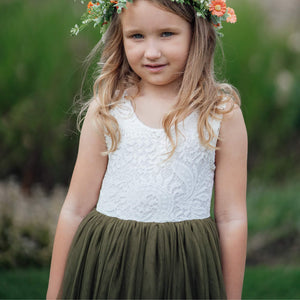 Young girl wearing a white lace top and green skirt with a floral crown outdoors.